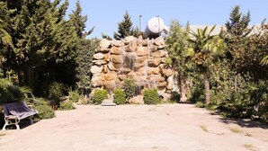 A rock formation with a water feature, surrounded by greenery and a bench. - Premier Villas (Baku)