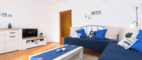 A modern living room with a sofa set, a television, and a small table with a blue cloth.