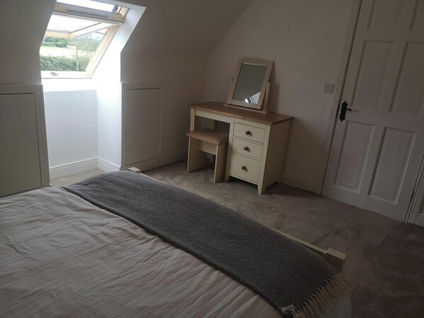 A bedroom with a bed, a desk with a mirror, a door, and a window. - 3 bed House With 2 Living Areas and 2 Bathrooms (Athy)