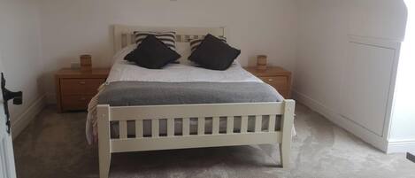 A bedroom with a white bed, two nightstands, a wooden dresser, and a sloped ceiling.