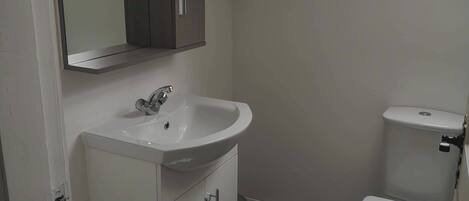 A bathroom with a white sink, a mirror above it, a toilet, and a window providing natural light.