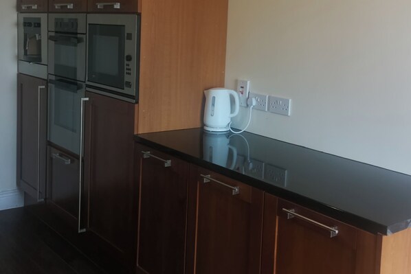 A kitchen with wooden cabinets, a black countertop, and a white kettle on the counter. - 3 bed House With 2 Living Areas and 2 Bathrooms (Athy)