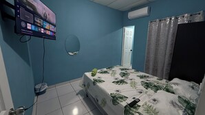 A bedroom with a bed, a TV mounted on the wall, a door, and a window with curtains.