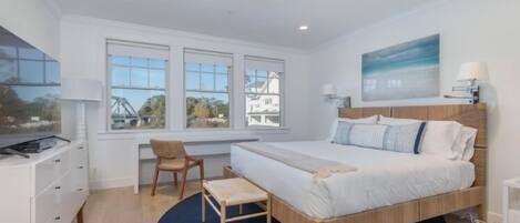 Un dormitorio con cama, una silla, un escritorio y una ventana que ofrece vistas a casas y un puente.