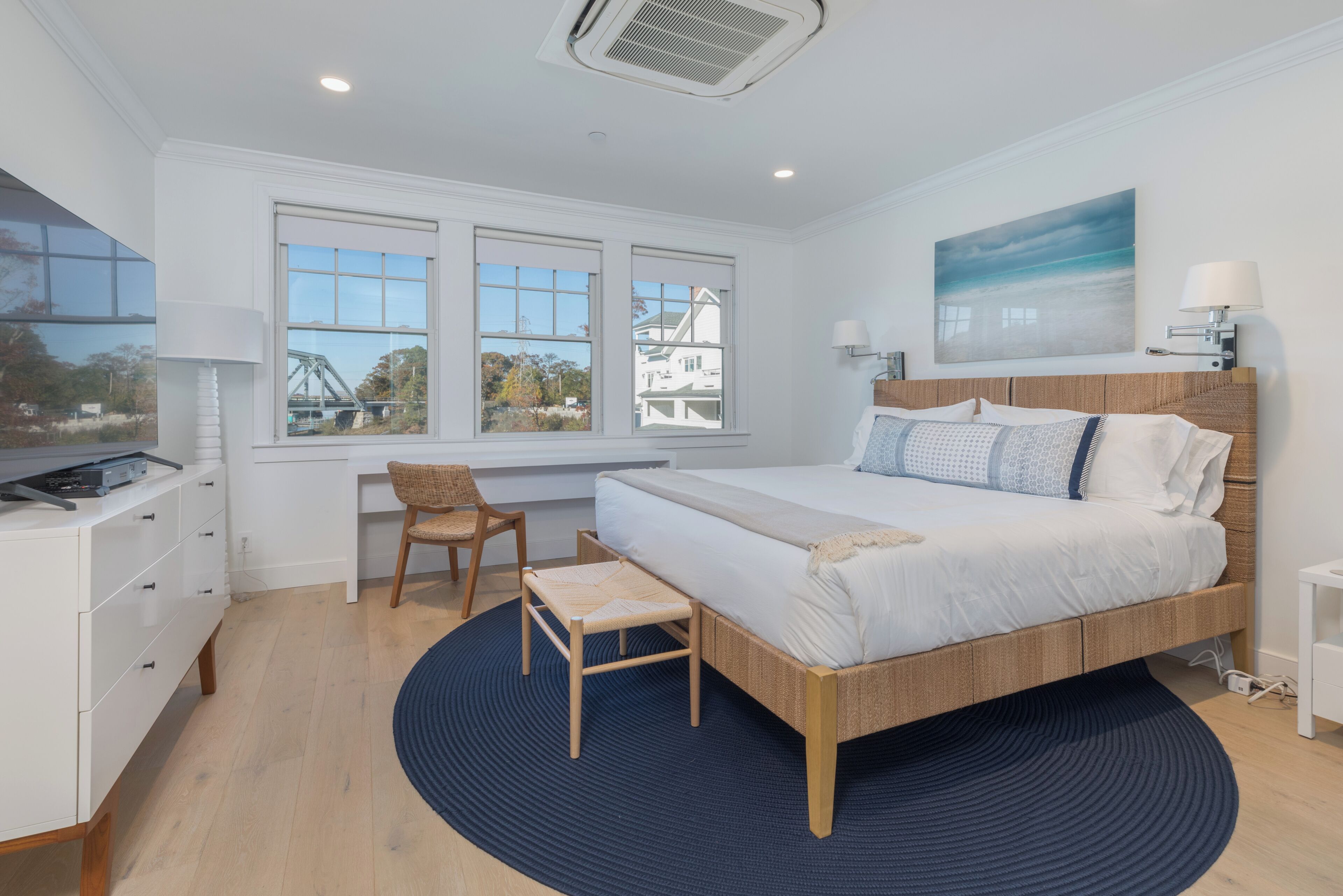 A bedroom with a bed, a desk, a chair, and a window with a view of a bridge.