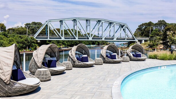 Zona de piscina con sillas de descanso y un puente al fondo.
