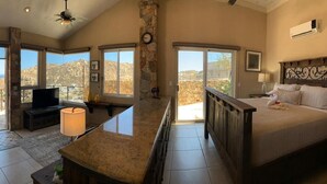 Un dormitorio espacioso con una cama grande, televisión y balcón con vistas a las montañas.