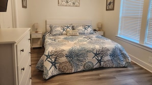 Un dormitorio con cama, cómoda, mesitas de noche y ventana con persianas.