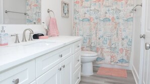 Un baño con tocador blanco, lavamanos, inodoro y cortina de ducha con motivos náuticos.