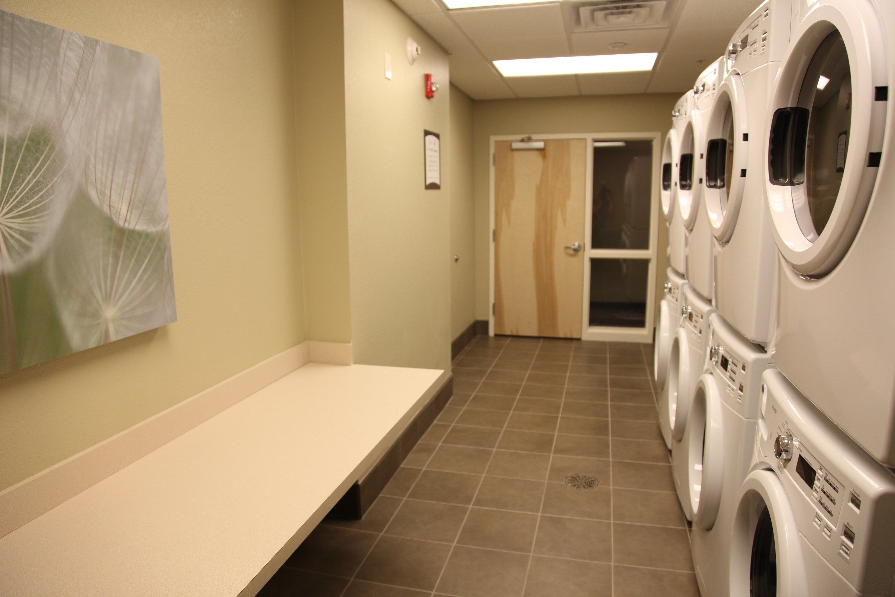 A laundry room with multiple washing machines, a bench, and a door leading to another room.