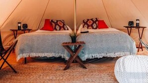 A cozy tent with a bed, pillows, a small table, and a woven rug. - Starlight Olympic (Port Angeles)