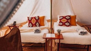 A cozy tent-style room with two beds, each with patterned pillows, a small table, and a brown chair. - Starlight Olympic (Port Angeles)