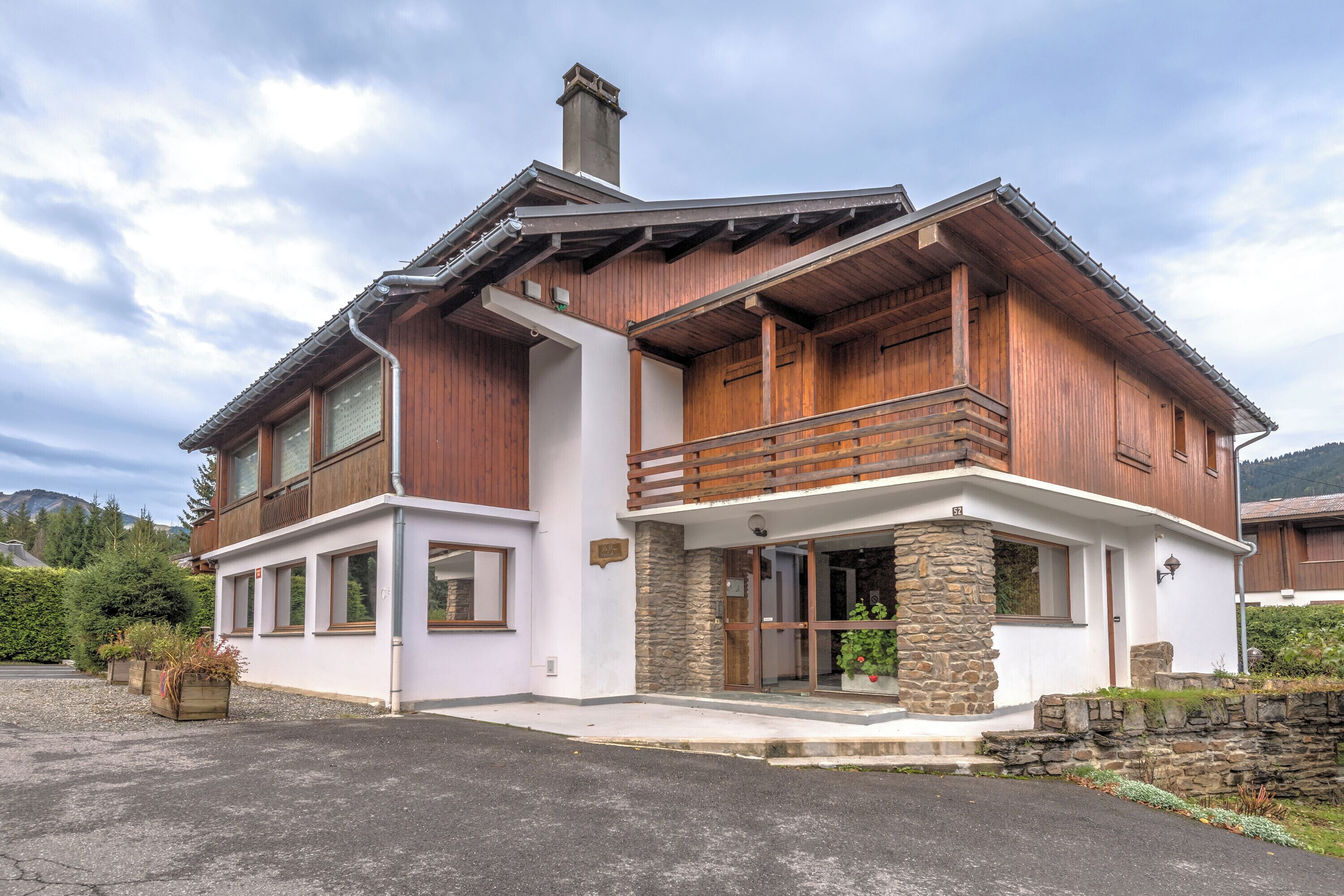 A two-story wooden house with a stone foundation, large windows, and a balcony.