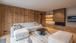 Un salon moderne avec un canapé d’angle, une table basse ronde et une cheminée intégrée.