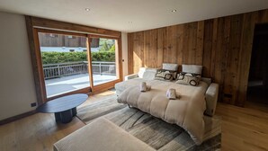 Une chambre avec un grand lit, des murs recouverts de panneaux de bois, une porte-fenêtre coulissante donnant sur un balcon et une petite table ronde.