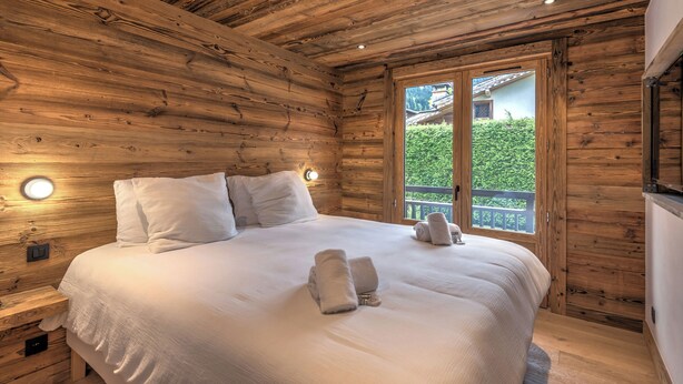 Une chambre dans une cabane en bois, avec un grand lit, du linge de lit blanc et une vue sur la verdure environnante.