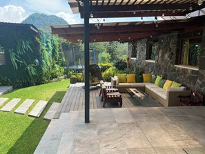An outdoor patio with a stone floor, a wooden pergola, and a seating area with cushions.