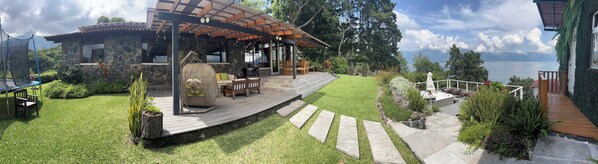 A covered outdoor area with a stone building, a wooden deck, and a view of a lake.