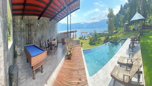 Zona de piscina con terraza de madera, mesa de billar y mobiliario exterior.