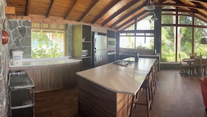 Una cocina amplia con una isla grande, techo de madera y vistas a exuberante vegetación.