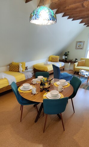 A dining area with a round table set for four, surrounded by teal chairs, in a room with yellow and blue furnishings.