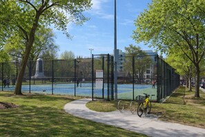 A fenced tennis court with a bicycle parked nearby, surrounded by trees and a clear sky.