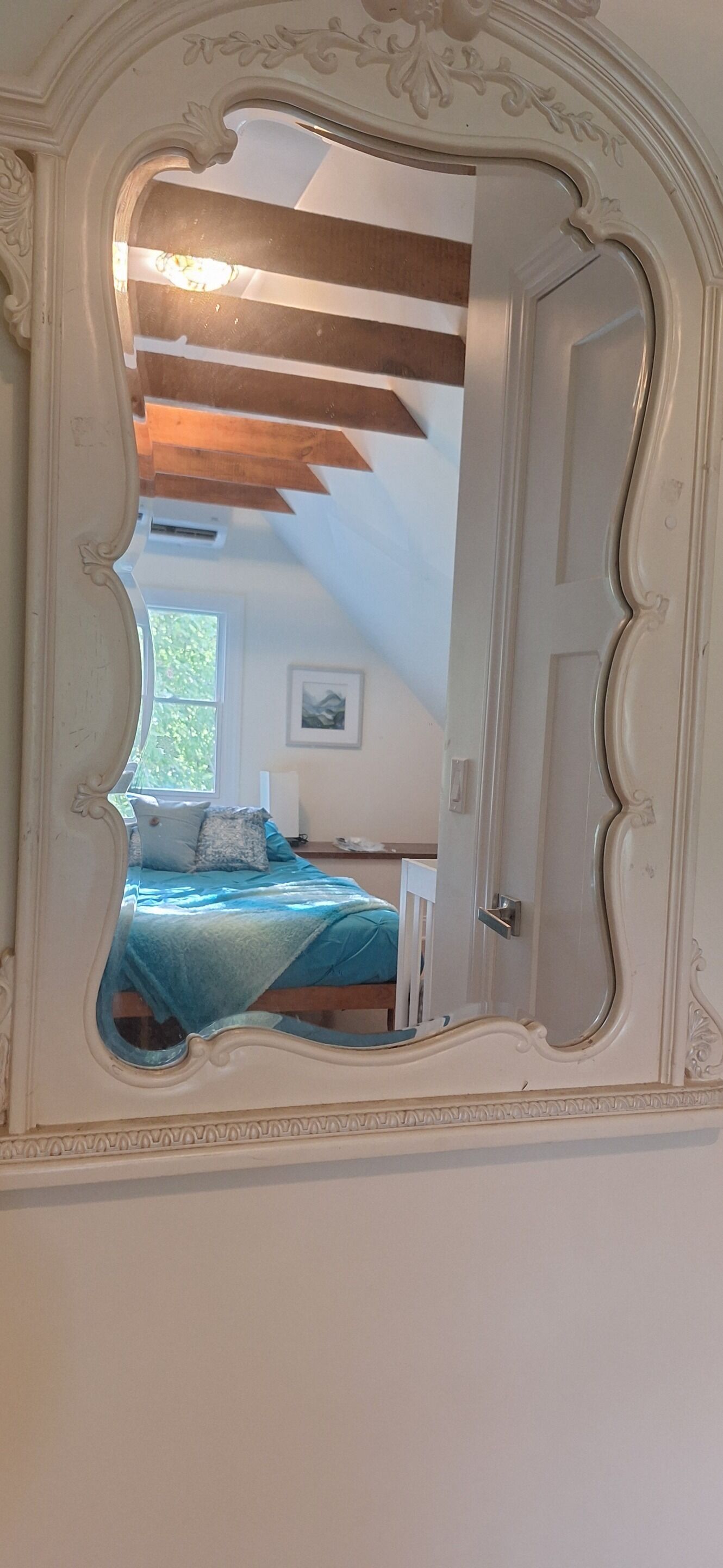 Une chambre à coucher avec un lit, une fenêtre et un miroir doté d’un cadre orné.