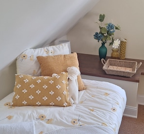 Una cama bien hecha con ropa de cama floral, una mesita de noche de madera con un florero y una cesta tejida.