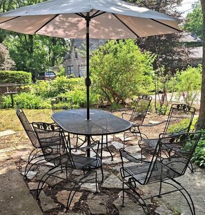 A patio with a round table and four chairs, an umbrella, and a stone-tiled floor.