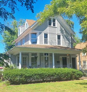 A two-story house with a porch, a chimney, and a brick wall.