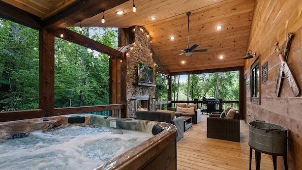 Eine Holzterrasse mit Whirlpool, Sitzgelegenheit und Kamin aus Stein.