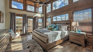 Ein geräumiges Schlafzimmer mit einem großen Bett, einem Holzkopfbrett und mehreren Fenstern mit Blick ins Freie.