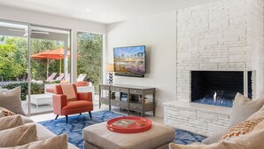 Una sala de estar moderna con chimenea, un televisor montado en la pared y un gran ventanal con vistas a un jardín.