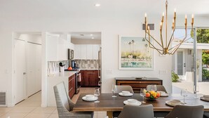 Un comedor moderno con una mesa de madera dispuesta para cuatro personas, una lámpara de araña y un cuadro en la pared.