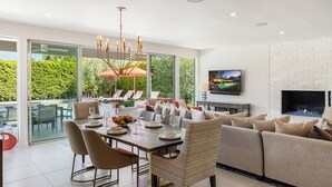 Una sala de estar moderna con chimenea, un comedor con una mesa dispuesta para cuatro personas, y un amplio ventanal con vistas a un jardín.