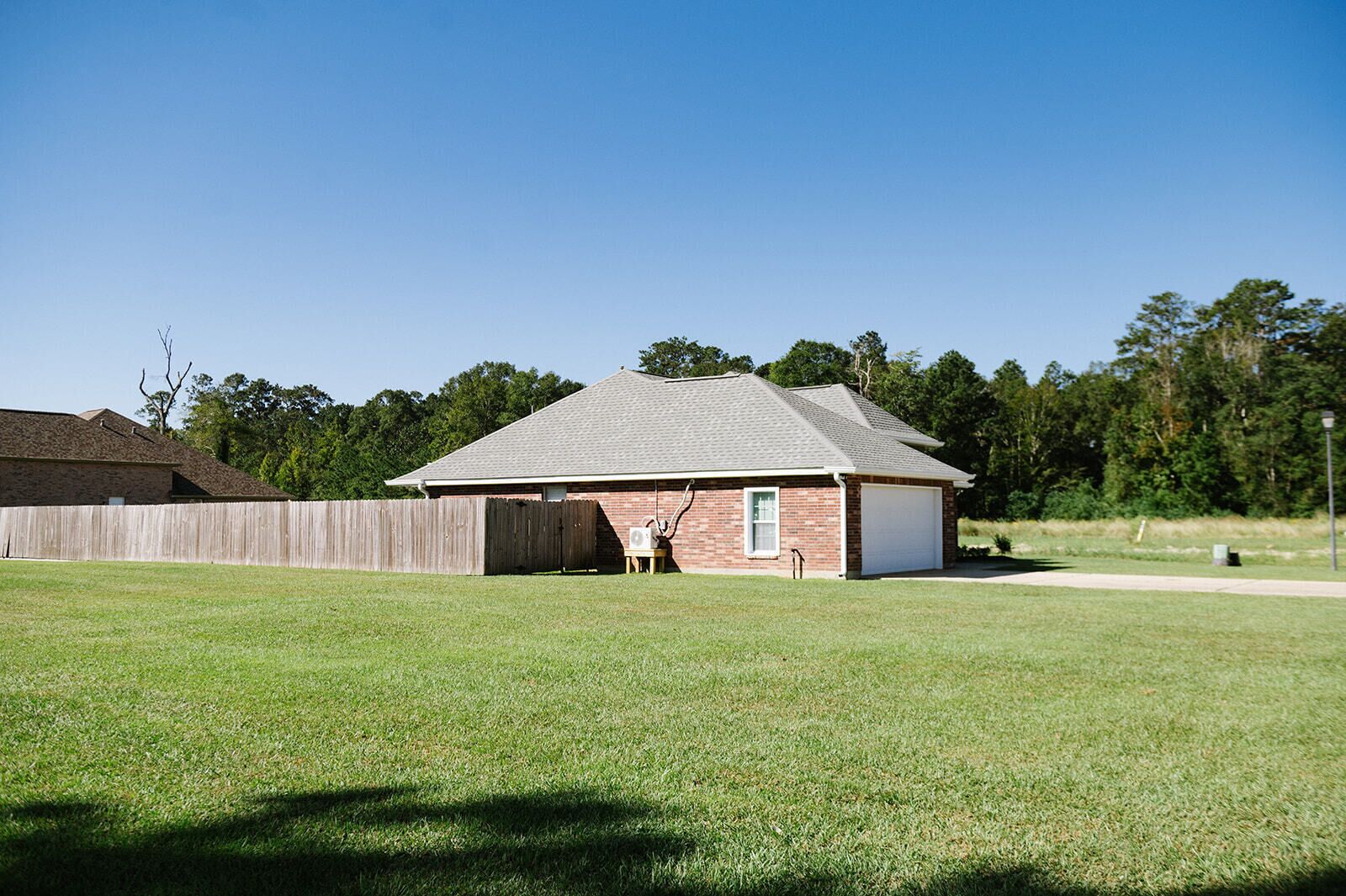 A single-story brick building with a white garage door, a wooden fence, and a well-maintained lawn.