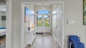 Un couloir avec une porte blanche donnant sur un balcon, une petite table avec une lampe et un porte-serviettes bleu.