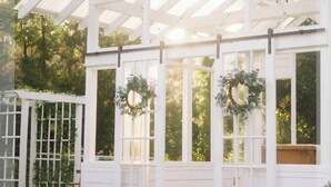 Un belvédère blanc doté d’un toit en verre, entouré de verdure et bordé d’un chemin en briques.