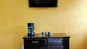 A black cabinet with drawers, a coffee maker, and a flat-screen TV mounted on a yellow wall. - Casa Flores (Tehuacán)