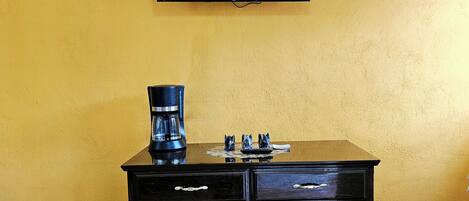 A black cabinet with drawers, a coffee maker, and a flat-screen TV mounted on a yellow wall.