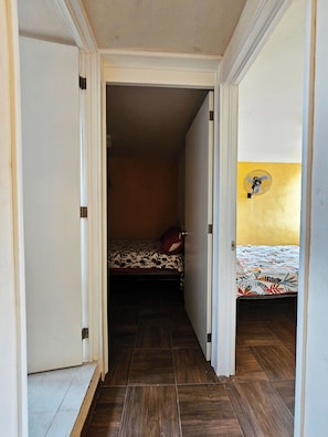 A narrow hallway leading to a bedroom with a bed and a fan. - Casa Flores (Tehuacán)