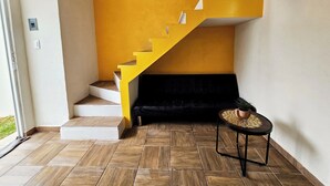 A staircase with yellow steps leading to a black sofa, a small round table with a plant, and a view of the outdoors through a glass door. - Casa Flores (Tehuacán)