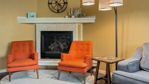 A living room with a fireplace, two orange armchairs, a grey sofa, and a table with a book. - Thistlebrook Rendezvous,Decks off each bedroom!  Backyard & Views!!! (Steamboat Springs)