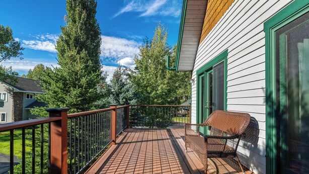 A wooden deck with a metal railing, a wicker chair, and a house with green trim and a white exterior. - Thistlebrook Rendezvous,Decks off each bedroom!  Backyard & Views!!! (Steamboat Springs)