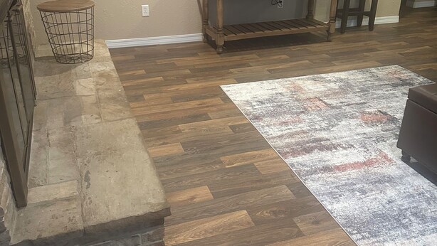 Un salon doté d’un parquet en bois disposé en motif «point de Hongrie», d’un téléviseur posé sur un meuble en bois, d’un tapis à motifs et d’un petit tabouret.