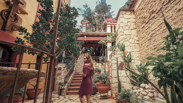 A woman walking in a courtyard with stone walls, potted plants, and a staircase. - Suites Amanecer by Casa del Sótano (Oaxaca)