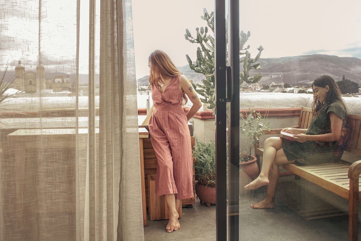 Un balcon donnant sur un paysage montagneux, un banc en bois et des plantes en pot.