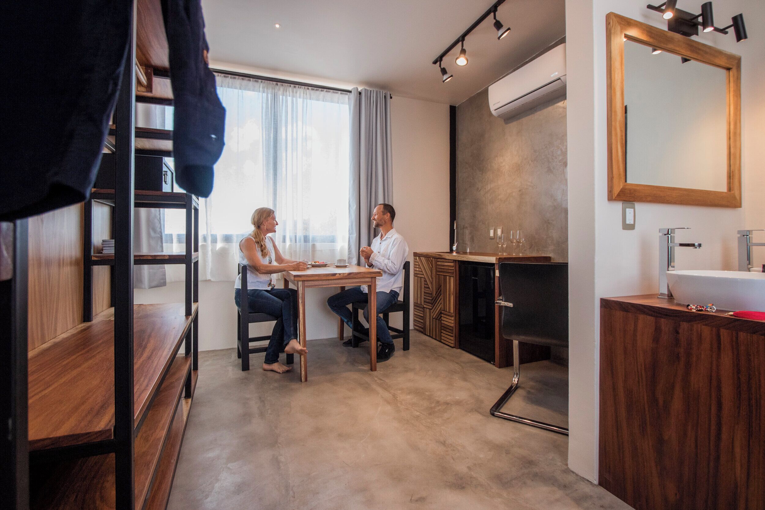 Une chambre moderne équipée d’un lit superposé, d’une table à manger, d’un coin cuisine et d’un grand miroir.