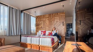 A modern bedroom with a large bed, a wooden headboard, a wooden bench, and a dining table. - Suites Amanecer by Casa del Sótano (Oaxaca)