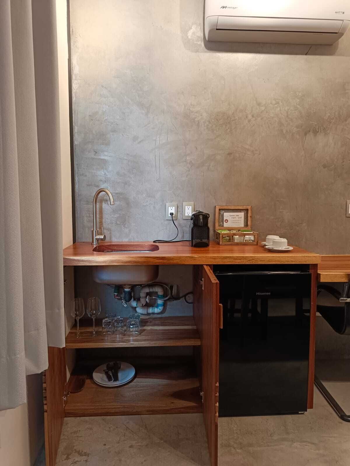 A compact kitchen with a sink, faucet, and countertop. There is a coffee maker and a framed certificate on the counter.